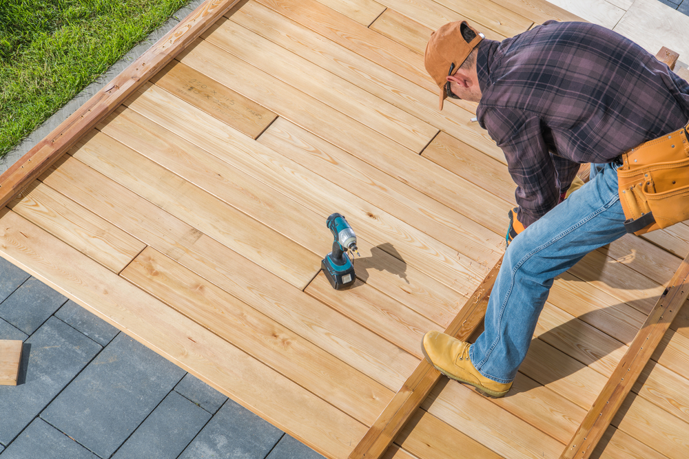 Professional constructing a deck with precision, using a drill and tools to secure wooden boards.