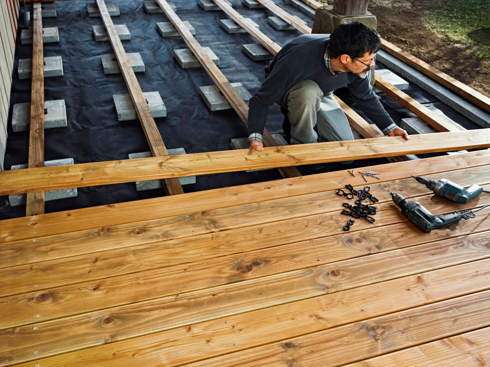 A homeowner installing a wooden deck with tools and fasteners, ensuring a smooth and secure deck installation.