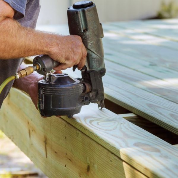 Worker using a nail gun to secure wooden boards during deck construction for a durable and safe structure.