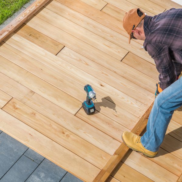 Professional constructing a deck with precision, using a drill and tools to secure wooden boards.