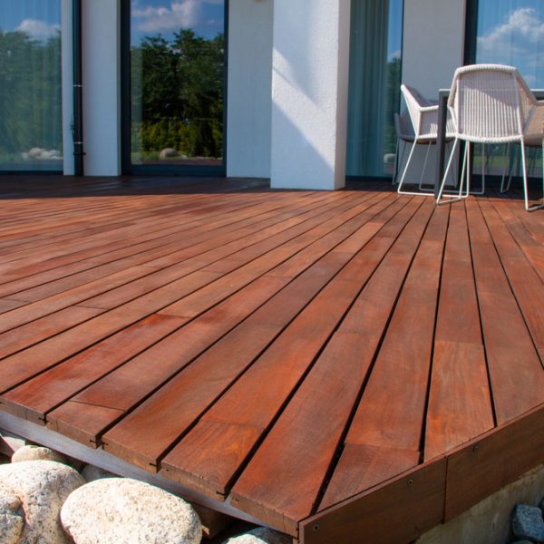 Freshly stained wooden deck with clean lines and an outdoor dining setup, demonstrating proper maintenance and repair techniques.